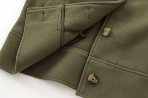 Détail macro de la veste en feutre vert armée montrant la laine épaisse et le bouton ambre