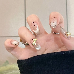 Close-up of nude gradient press-on nails with black polka dots and gold bow accents