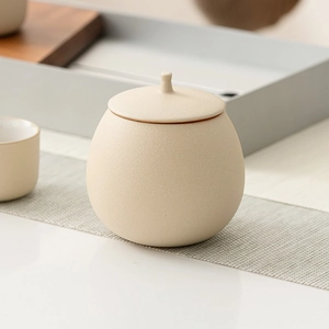 Beige ceramic tea storage canister with a matte finish on a wooden tea tray