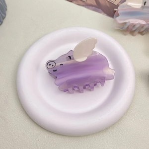 Cute purple pig-shaped acetate hair claw clip with white wings on a white display plate