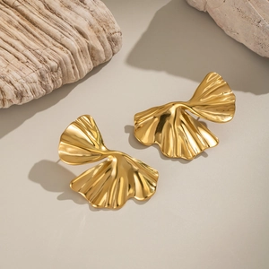 Macro detail of 18K gold ginkgo leaf earrings on rustic wood with polished wave texture