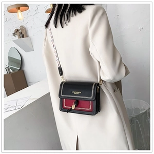 Detail of cross-body bag in black and red contrast with gold hardware and woven strap