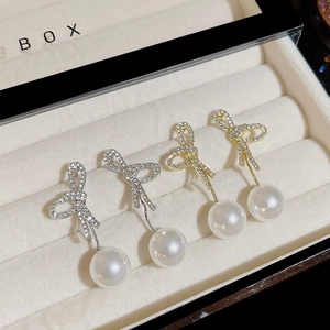 Elegant bow knot pearl drop earrings in gold and silver finish displayed in a jewelry box