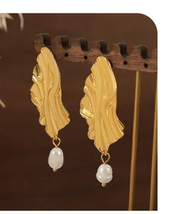 Gros plan de boucles d'oreilles dorées à texture ondulée et perles d'eau douce blanches