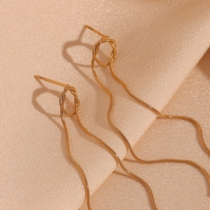 Macro detail of golden knotted snake chain tassel earrings on elegant beige silk fabric