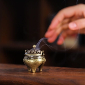 Antique bronze tripod incense burner with hollow carved lid and rising smoke on wood