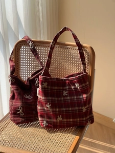 Détail du sac cabas à carreaux rouges avec broderies de nœuds blancs sur une chaise