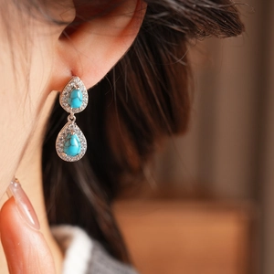 Close-up of vintage silver earrings with turquoise resin drops and zircon accents