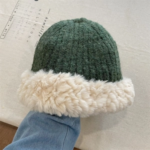 Close-up of thick green knit texture and beige faux fur brim on winter beanie hat