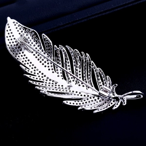 Macro shot of silver feather brooch with clear zircons on dark leather texture