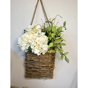 Detail of woven door basket with white hydrangeas and green leaves on hemp rope