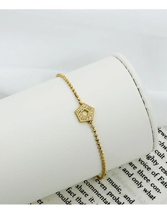 Detail view of gold beaded bracelet with zircon-encrusted hexagonal charm on a stand
