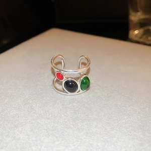 Close-up of adjustable silver open ring with red, black, and green oval gemstones