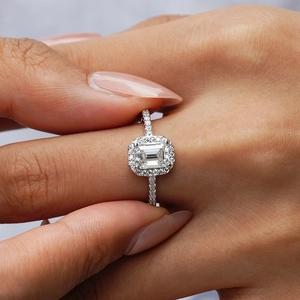 Luxury emerald cut S925 silver ring with halo moissanite, shown held by fingertips