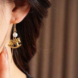 Detailed view of a golden rocking horse earring with pearl accent on ear model
