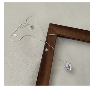 Detailed macro of S925 sterling silver heart necklace with blue zircon on wooden frame
