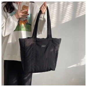 Detail of a black quilted nylon tote bag with polished metal logo plaque and soft texture