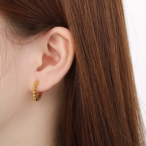 Close-up of a woman wearing gold beaded hoop earrings in minimalist polished stainless steel