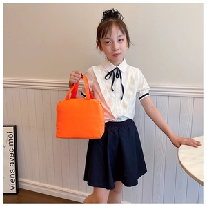 Detail of a bright orange canvas insulated lunch bag held by a girl in an indoor setting