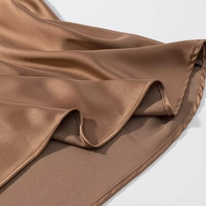 Macro detail of bronze satin asymmetric dress showing premium stitching and fabric drape