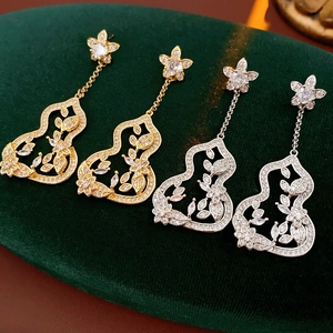 Détail de boucles d'oreilles fleur et gourde en or et argent sur velours vert