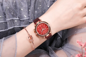 Détail d'une montre rouge ciel étoilé avec bracelet magnétique et jonc doré à noeud