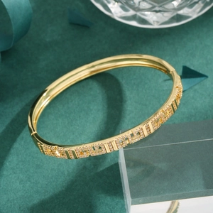 Elegant gold bangle featuring geometric cutouts and paved white zircon on dark green background