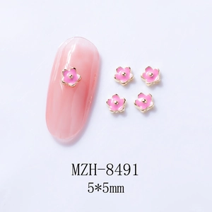 Macro detail of 5x5mm pink flower nail art charms with golden edges on manicured nails