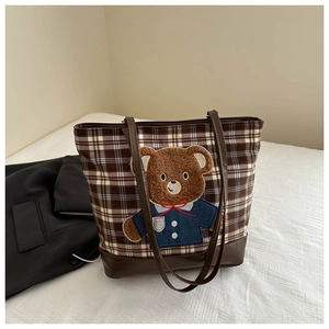 Detail of a brown plaid tote bag featuring a cute 3D bear embroidery and faux leather base