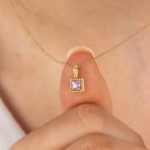 Macro shot of small purple square zircon pendant on a gold stainless steel necklace chain