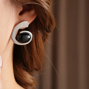 Close-up of silver abstract C-shape earrings with a large black oval gemstone on model