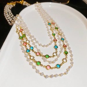 Close-up of multi-layer pearl necklace with colorful gemstones on a white tray