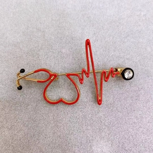 Close-up of golden stethoscope and heartbeat brooch with red enamel and crystal