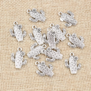 Collection of silver alloy cactus pendants with flower details on rustic burlap fabric