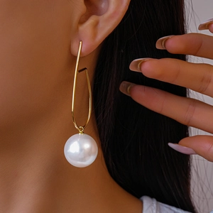 Dettaglio orecchini geometrici dorati con grande perla bianca indossati da una modella