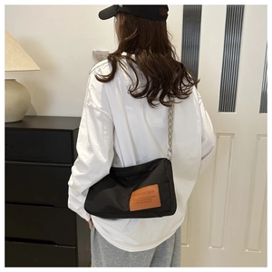 Detailed view of black nylon crossbody bag featuring a patterned wide strap and brown leather patch
