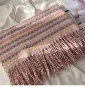 Macro detail of soft pastel plaid scarf featuring long decorative tassel fringe edges
