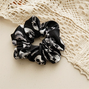 Detail of satin Halloween hair scrunchie featuring white skull prints on black fabric