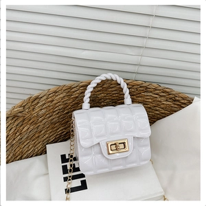 Quilted white jelly bag with twisted handle and gold chain strap on beach hat and book