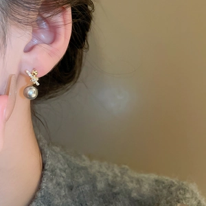 Close-up of a gold bow earring with crystals and a grey pearl on a female model