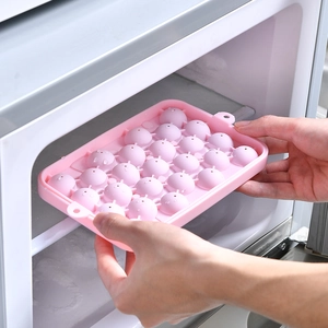 Pink silicone ice ball mold with lid being placed into freezer for round ice cubes