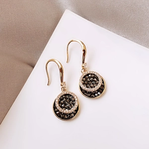 Detail of gold drop earrings with black center and white crystals pave setting