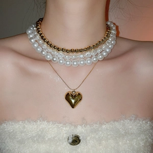 Détail de colliers superposés avec pendentif cœur doré et perles sur le cou