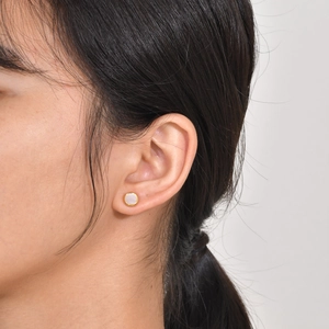 Close-up of minimalist gold zircon stud earring with white inlay on female model