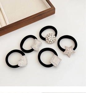 Flat lay of black elastic hair ties with rhinestone hearts, bows, and pearls on white background