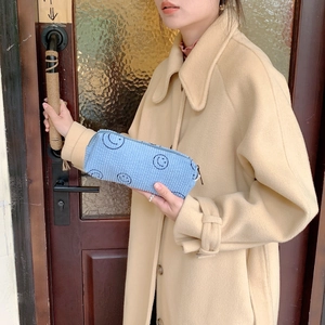 Detail of light blue corduroy cosmetic bag with black smiley faces held by a model