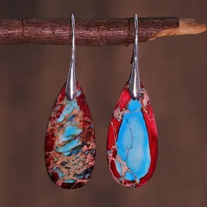 Macro detail of teardrop natural stone earrings with red and blue textures on wood