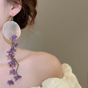 Detail of asymmetric purple floral tassel earrings with translucent shell discs on model