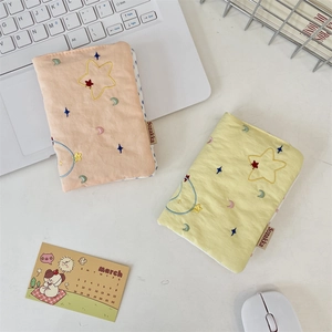 Close-up of star and moon embroidery on cotton passport holders in pastel orange and yellow