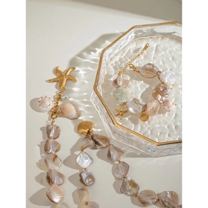 Detailed close-up of 18k gold starfish and seashell charms on a pearl shell necklace